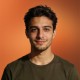 Smiling young man with short dark hair, portrait on orange background